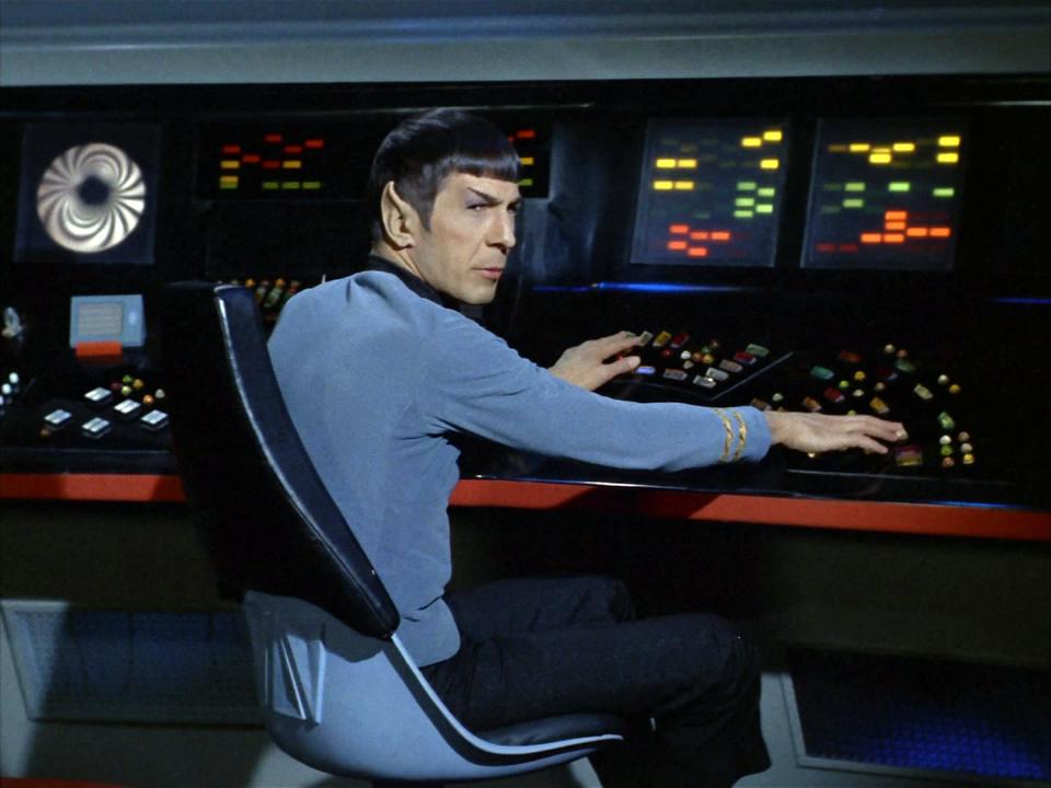 Leonard Nemoy as Spock sits at a command desk on the set of TV show Star Trek