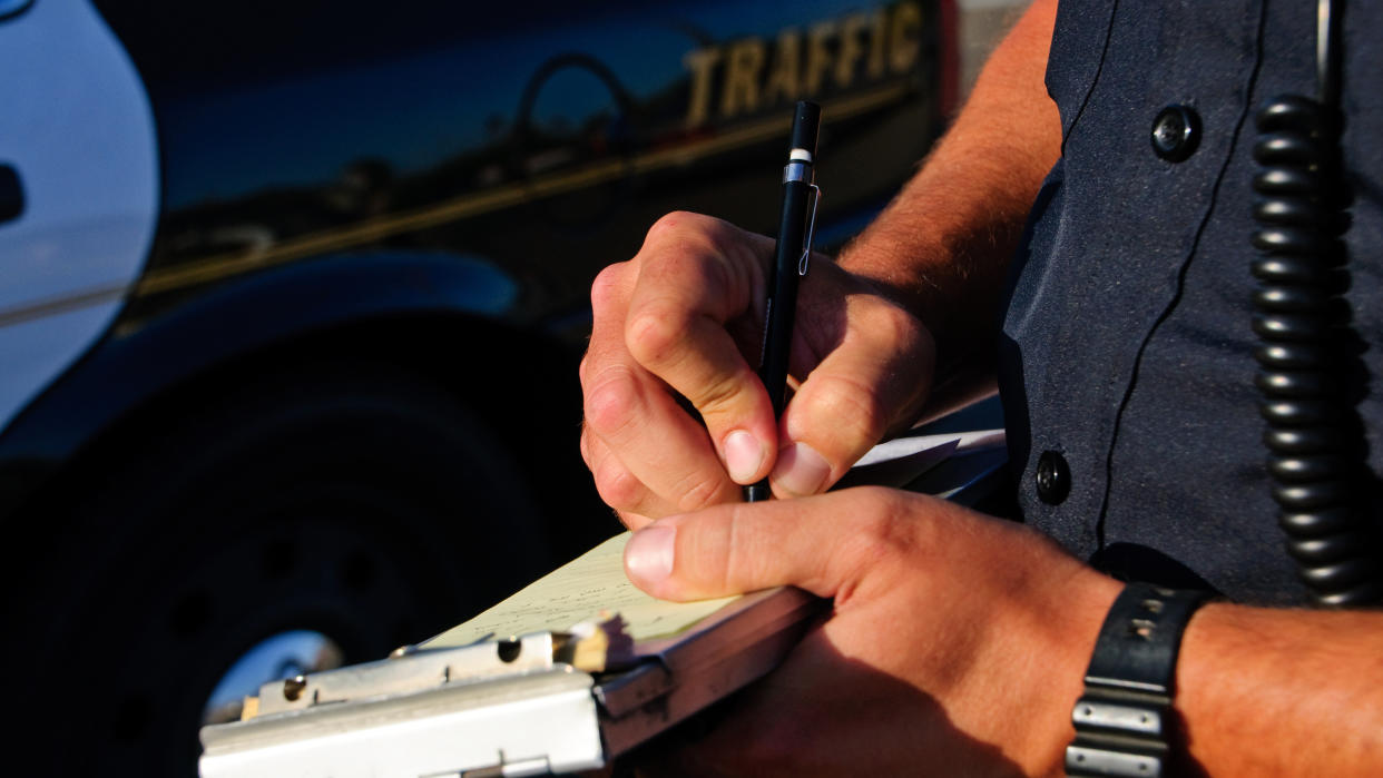 A police officer standing next to a patrol car writes a ticket. (iStockphoto/Getty Images)