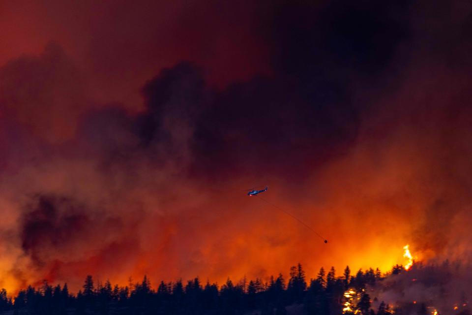 TOPSHOT - A helicopter battles the McDougall Creek wildfire as it burns in the hills West Kelowna, British Columbia, Canada, on August 17, 2023, as seen from Kelowna. Evacuation orders were put in place for areas near Kelowna, as the fire threatened the city of around 150,000. Canada is experiencing a record-setting wildfire season, with official estimates of over 13.7 million hectares (33.9 million acres) already scorched. Four people have died so far. (Photo by Darren HULL / AFP) (Photo by DARREN HULL/AFP via Getty Images)