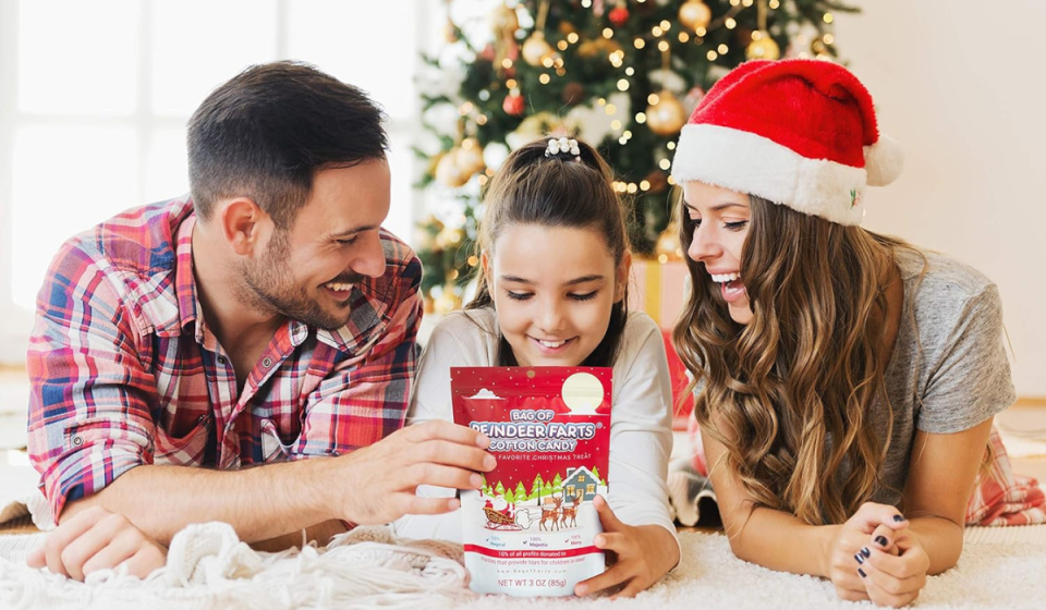 father and mother giving back of 'Reindeer Farts' to daughter in front of Christmas tree