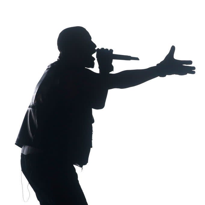 Silhouetted performer with a microphone extends hand outward on stage