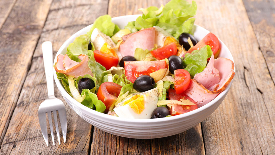 Salad topped with boiled eggs, ham, tomatoes and olives
