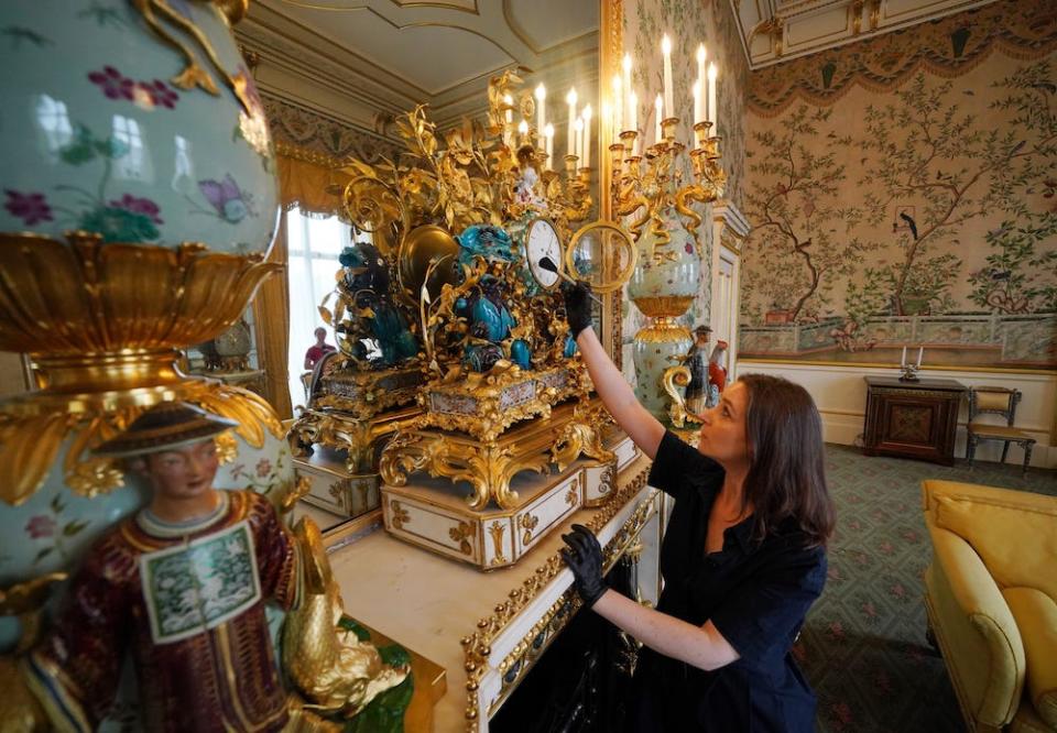 Una donna rispolvera un orologio d'oro e turchese riccamente decorato, noto come Cailin Clock, su una mensola del camino durante gli ultimi ritocchi alla ristrutturazione dell'ala est di Buckingham Palace, l'8 luglio 2024.