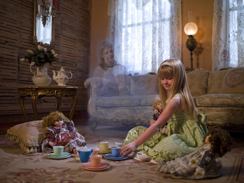 Girl having a tea party with dolls, ghostly figure in background, vintage room setting