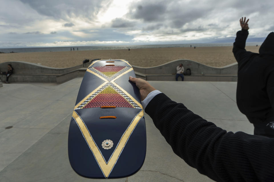 Di'Orr Greenwood, an artist born and raised in the Navajo Nation in Arizona and whose artwork is featured on the new U.S. stamps, shows one of her skateboards designs in the Venice Beach neighborhood in Los Angeles Monday, March 20, 2023. On Friday, March 24, the U.S. Postal Service is debuting the "Art of the Skateboard," four stamps that will be the first to pay tribute to skateboarding. The stamps underscore how prevalent skateboarding has become, especially in Indian Country, where the demand for designated skate spots has only grown in recent years. (AP Photo/Damian Dovarganes)