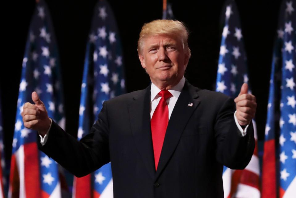 Donald Trump with thumbs up in front of American flags