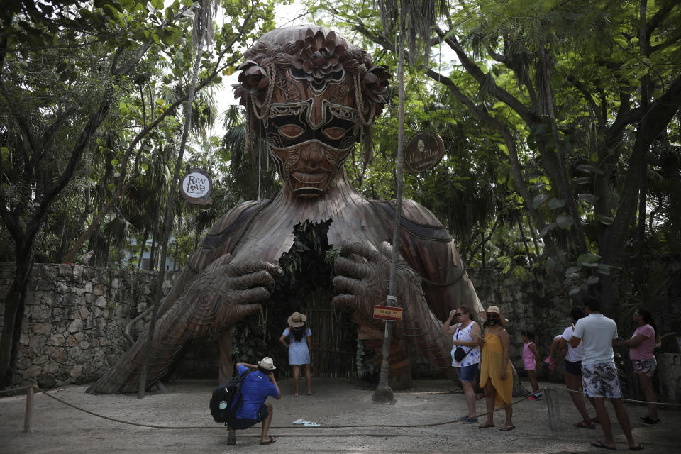 Tourists wait their turn to pose for a photo with a figurative sculpture that serves as an archway by South African artist Daniel Popper titled, "Ven a la Luz" at the Ahau Tulum resort, Quintana Roo state, Mexico, Monday, Jan. 4, 2021. Concern is spreading that the winter holiday bump in tourism could be fleeting because it came as COVID-19 infections in both Mexico and the United States were reaching new heights. (AP Photo/Emilio Espejel)