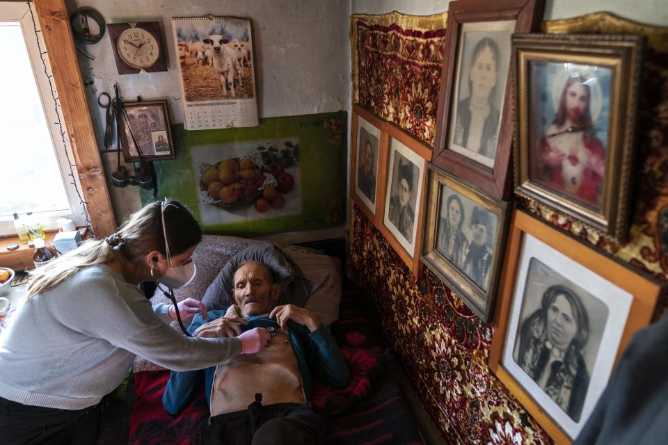 Dr. Viktoria Mahnych, wearing face mask against coronavirus, checks on a COVID-19 patient with a stethoscope at at his home in Iltsi village, Ivano-Frankivsk region of Western Ukraine, Wednesday, Jan. 6, 2021. Ukraine is struggling to contain the coronavirus pandemic that has inundated its overburdened medical system, as Dr. Viktoria Mahnych goes door to door providing much needed help to patients.(AP Photo/Evgeniy Maloletka)