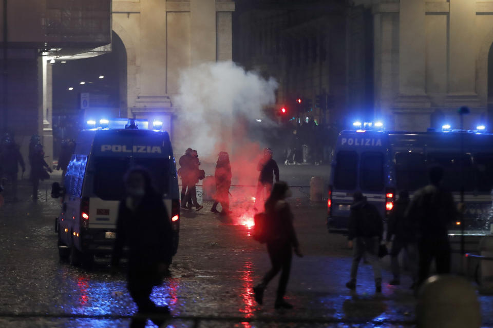 Police officers stand by burning flares during a protest against the government restriction measures to curb the spread of COVID-19, in Rome Tuesday, Oct. 27, 2020. Italy's leader, Premier Giuseppe Conte, has imposed at least a month of new restrictions to fight rising coronavirus infections, shutting down gyms, pools and movie theaters and putting an early curfew on cafes and restaurants. (AP Photo/Alessandra Tarantino)