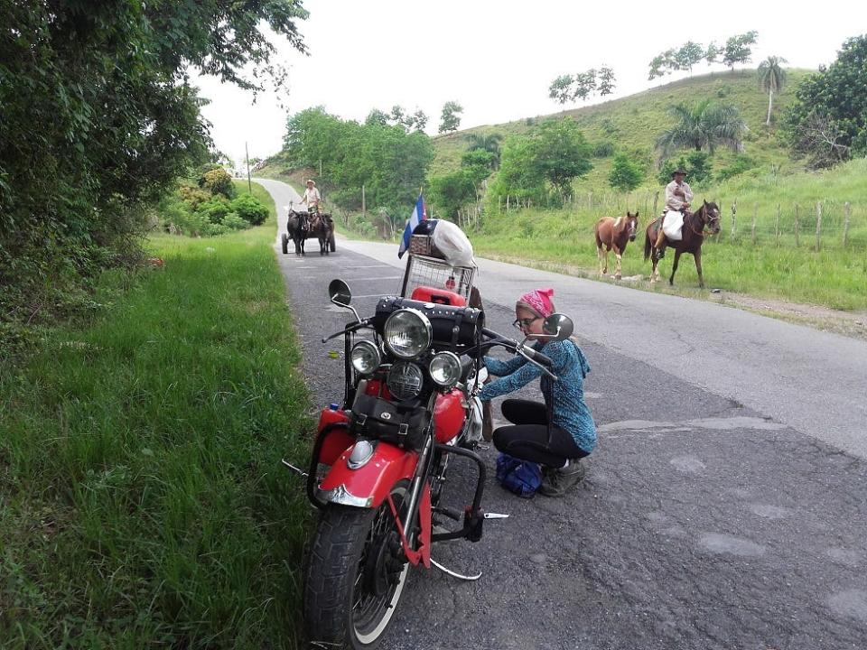 Woman on the road in Cuba with motorbike and horses walking in the background