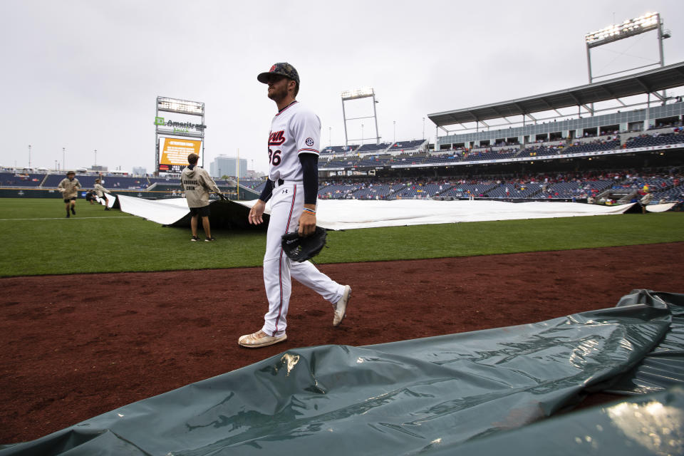 Auburn's Kyle Gray walks past the grounds crew as they tarp in infield at the fourth inning. (Ryan Soderlin/Omaha World-Herald via AP)