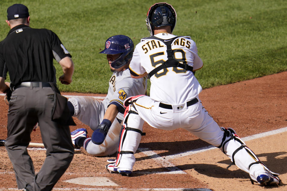 Milwaukee Brewers' Keston Hiura, center, is tagged out by Pittsburgh Pirates catcher Jacob Stallings (58) with umpire Junior Valentine making the call during the third inning of a baseball game in Pittsburgh, Saturday, July 3, 2021. (AP Photo/Gene J. Puskar)