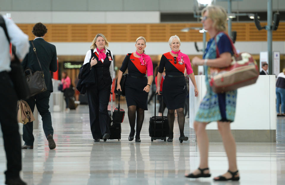 Qantas staff (C) walk through the terminal of Sydney domestic airport on 27 February, 2014. Struggling Australian carrier Qantas February 27 said it will axe 5,000 jobs, defer aircraft deliveries and freeze growth at Asian offshoot Jetstar in a major shake-up after deep first-half losses, warning of more pain to come.   AFP PHOTO/William WEST        (Photo credit should read WILLIAM WEST/AFP via Getty Images)