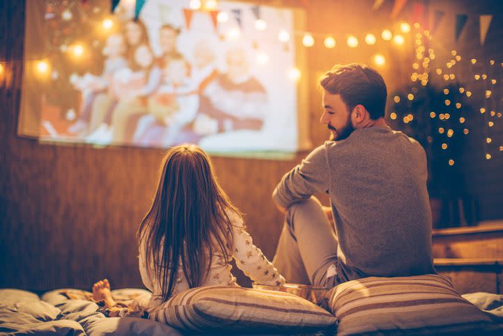 father and daughter sitting at backyard and looking movie at home improved theatre backyard is decorated with string lighs