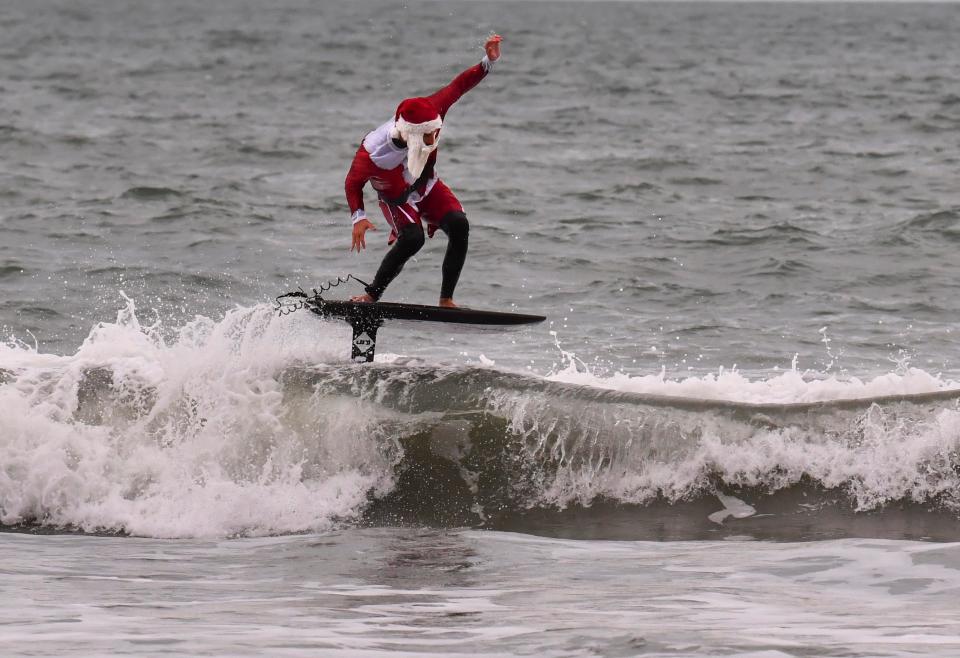 Gordon Harrison doing some foil surfing in his Santa oufit.  George Trosset getting ready for the 14th Surfing Santa event Christmas Eve in Cocoa Beach. 