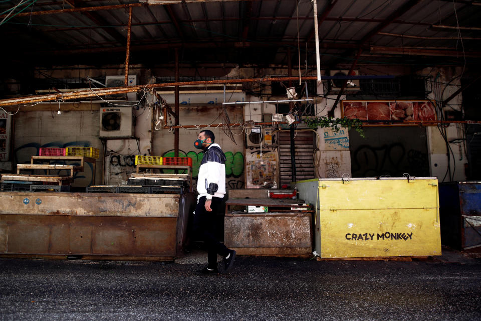 FILE PHOTO: A man wearing a face mask walks past shuttered stalls at a market as Israel tightened a national stay-at-home policy with guidelines aimed at halting the spread of the coronavirus, in Tel Aviv, Israel