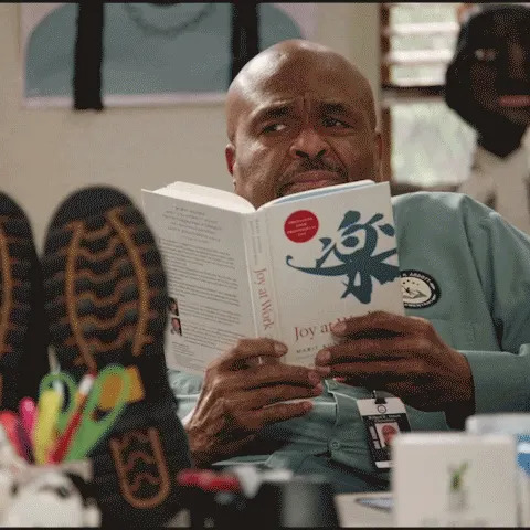 Mr. Johnson from Abbott Elementary reading a book with his feet up on a desk