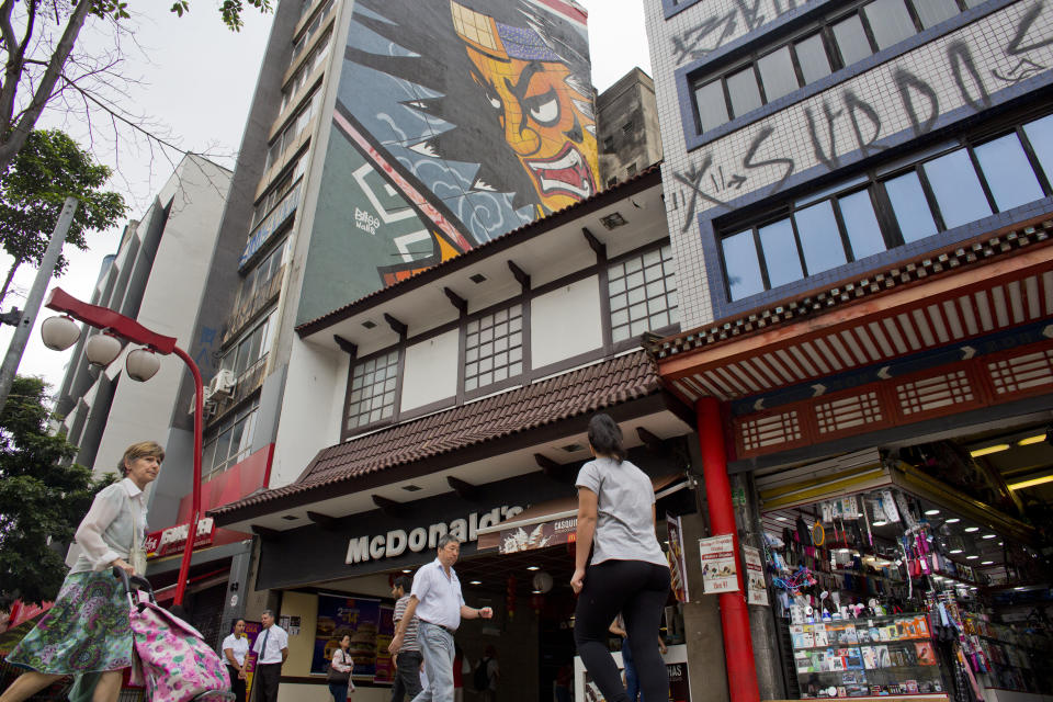 In this Dec. 27, 2018 photo, people walk under a mural of a Samurai in Sao Paulo, Brazil's Asian neighborhood of Liberdade, the area where an influential Japanese-language newspaper ran its last print edition on Jan. 1, 2019. Japanese immigrants introduced foods that changed Brazilian cuisine and farming techniques that helped turn Latin America's biggest country into an agricultural superpower. (AP Photo/Victor R. Caivano)