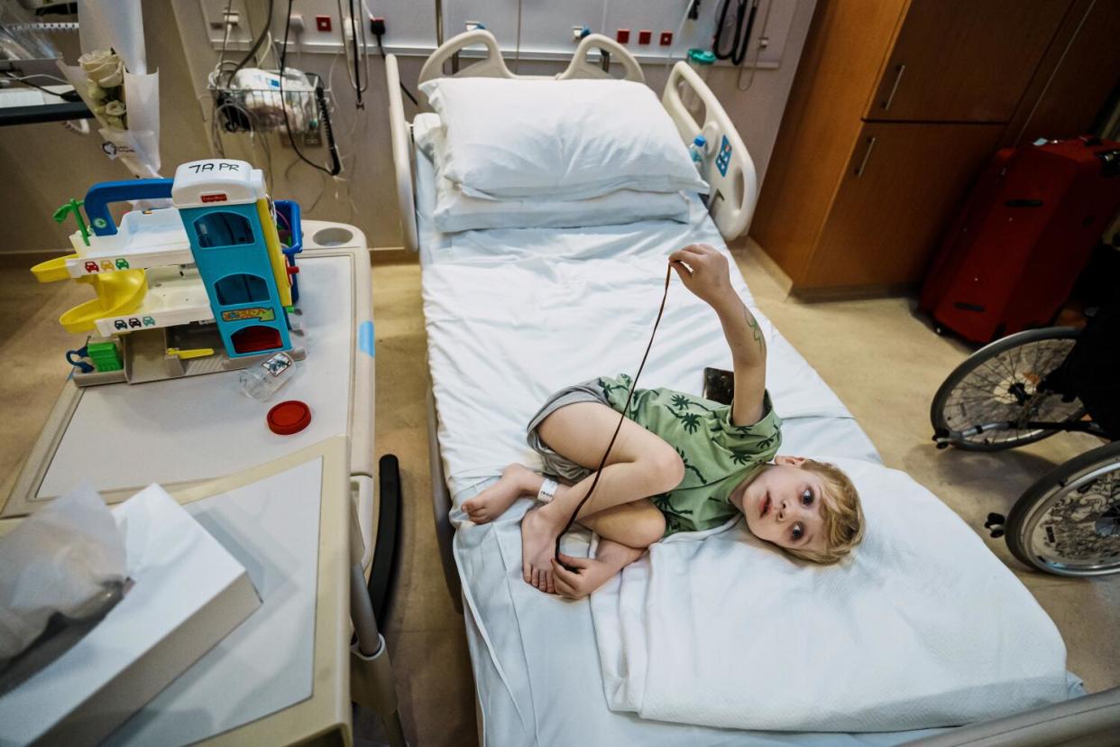 A 5-year-old curls up at the foot of a hospital bed