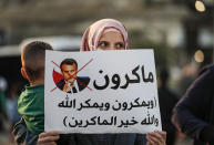 An Arab Israeli Muslim demonstrator, holding a child and clad in mask due to the COVID-19 coronavirus pandemic, holds up a sign during a rally protesting against the comments of French President Emmanuel Macron over Prophet Mohammed cartoons, in the Arab town of Umm-Al Fahem in Northen Israel on October 25, 2020. (Photo by Ahmad GHARABLI / AFP) (Photo by AHMAD GHARABLI/AFP via Getty Images)