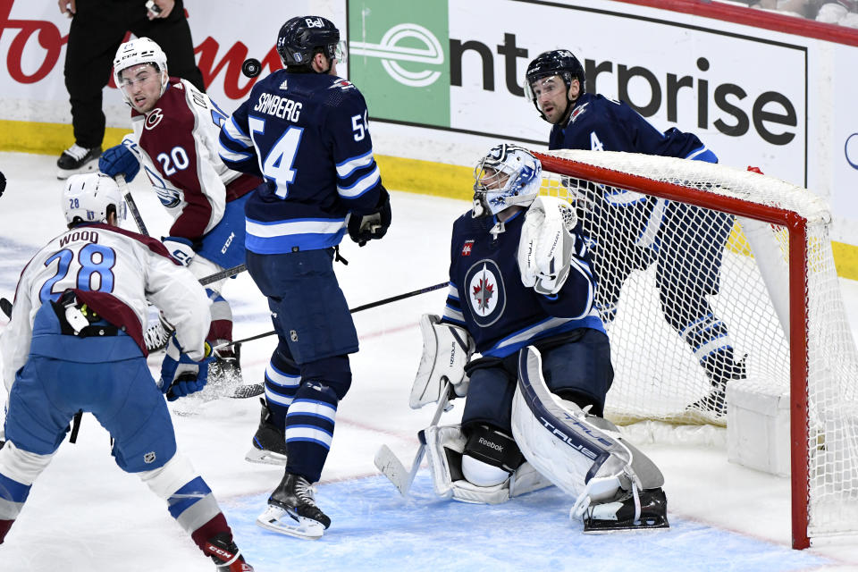 Winnipeg Jets' goaltender Connor Hellebuyck (37) and teammates Neal Pionk (4) and Dylan Samberg (54) keep their eyes on a bouncing puck, as do Colorado Avalanche's Ross Colton (20) and Miles Wood (28) during the third period in Game 2 of an NHL hockey Stanley Cup first-round playoff series Tuesday, April 23, 2024, in Winnipeg, Manitoba. (Fred Greenslade/The Canadian Press via AP)