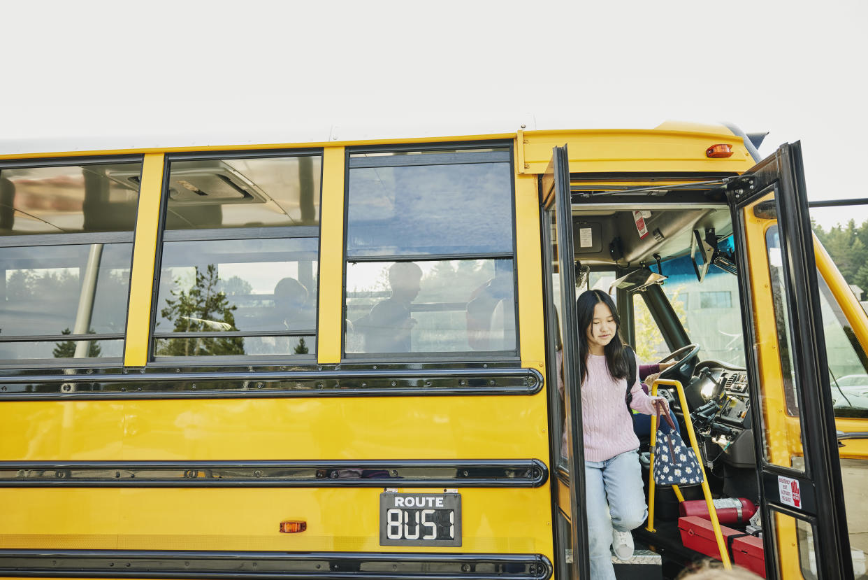 Wide shot of smiling middle school students disembarking a school bus.