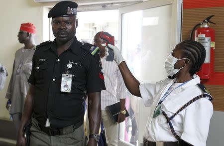 An immigration officer uses an infra-red laser thermometer to examine a policeman on his arrival at Nnamdi Azikiwe International Airport in Abuja, August 11, 2014. REUTERS/Afolabi Sotunde