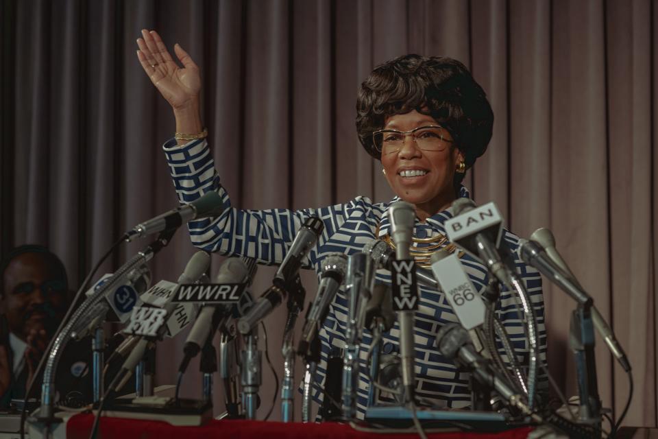 a woman (regina king as shirley chisolm) waves in front of a group of microphones