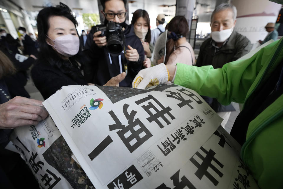 An employee hands over the copies of extra edition of the Yomiuri Shimbun newspaper reporting Japan won over the U.S. at the final of the World Baseball Classic (WBC), Wednesday, March 22, 2023, in Tokyo. The headline of the newspaper said "Japan, Number one in the world." (AP Photo/Eugene Hoshiko)