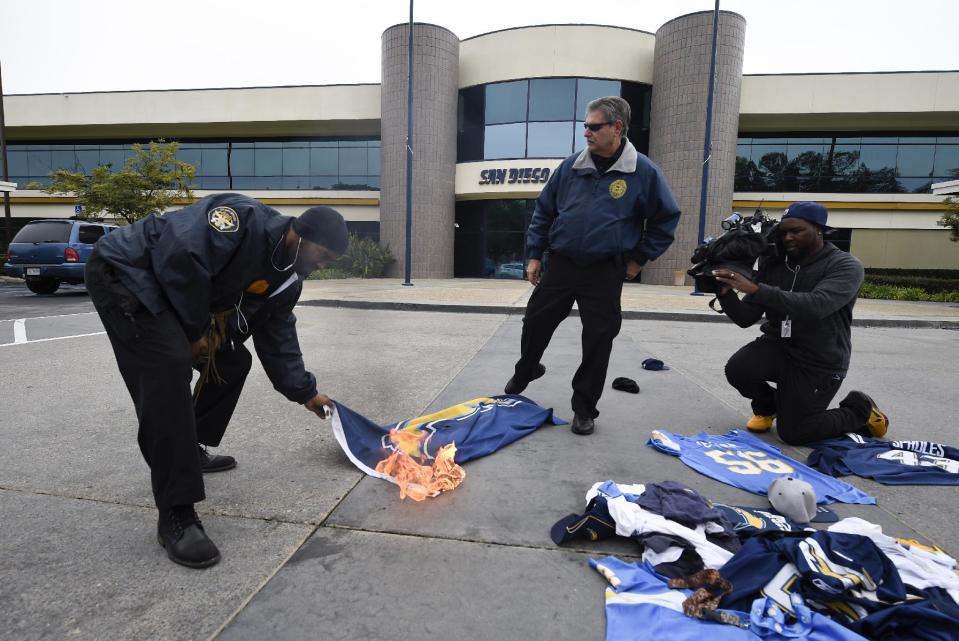 A security guards puts out the fire started by a fan on a burning San Diego Chargers flag in front of Chargers headquarters after the team announced that it will move to Los Angeles, Thursday Jan. 12, 2017, in San Diego. (AP Photo/Denis Poroy)