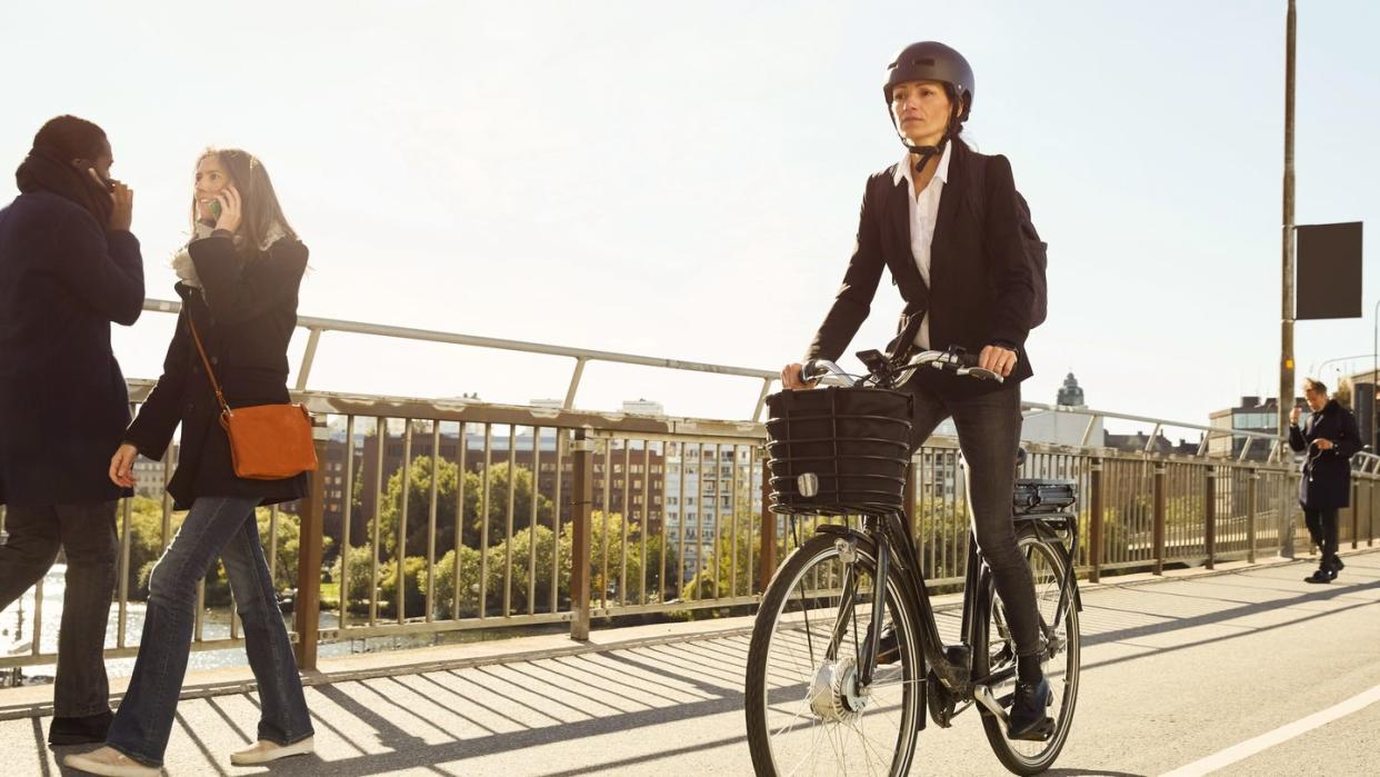 mature woman riding electric bicycle by commuters on bridge in city against sky