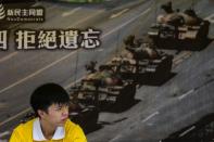 An activist sits in front of a poster of the "Tank Man" photo at his stall in Hong Kong on June 4, 2016, ahead of the commemoration of the Tiananmen Square crackdown in 1989