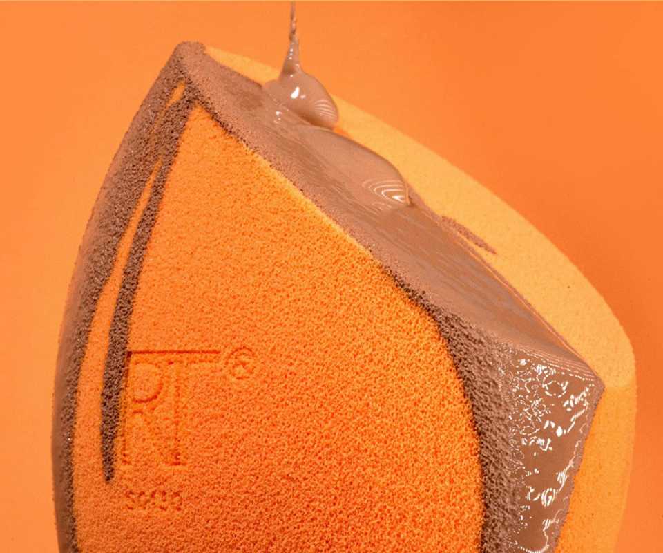 A close up of the orange beauty sponge with foundation dripping over it against a dark orange backdrop.