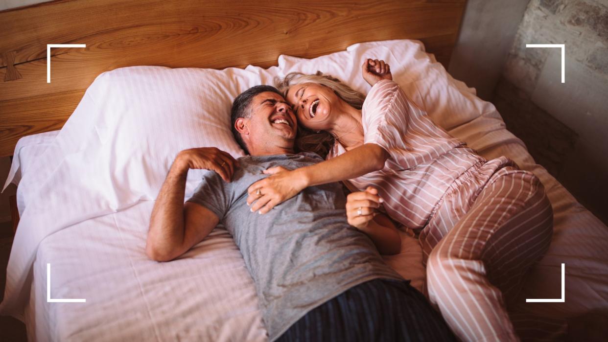  Couple lying in bed together laughing, illustrating the downward dog sex position 