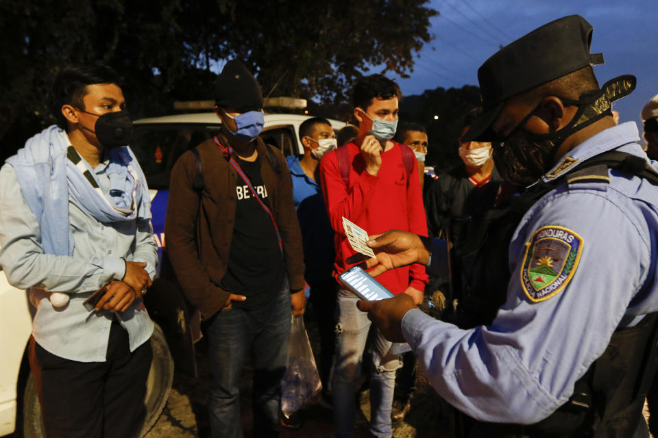 Un policía verifica los documentos de migrantes el jueves 14 de enero de 2021 antes de permitirles seguir rumbo a la frontera en la carretera que va a Choloma desde San Pedro Sula, Honduras. (AP Foto/Delmer Martínez)