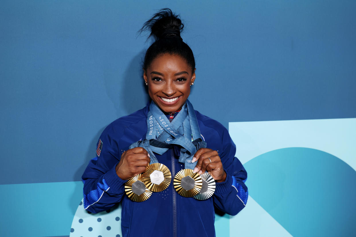 Simone Biles smiles as she holds up her four medals from the Paris Olympics.