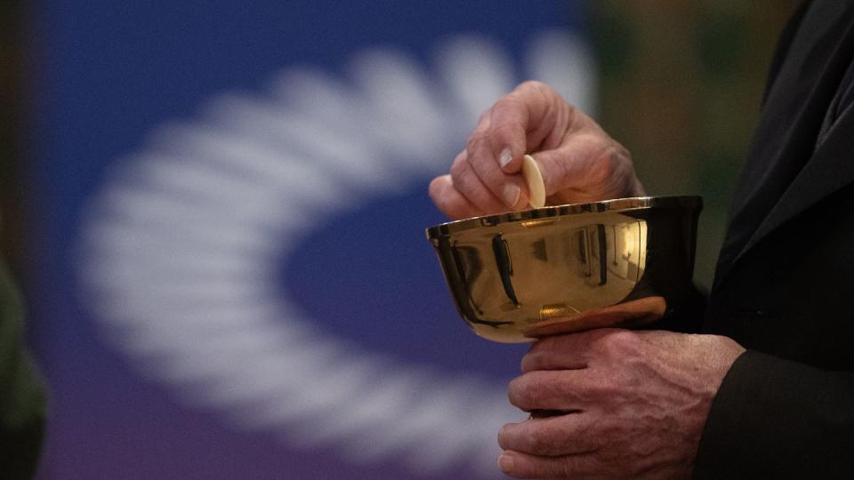 Ein Mitglied der Kirchengemeinde hält während eines Gottesdienstes mit Abendmahl im katholischen Dom St. Bartholomäus vor dem Logo des ÖKT eine Oblate in der Hand.