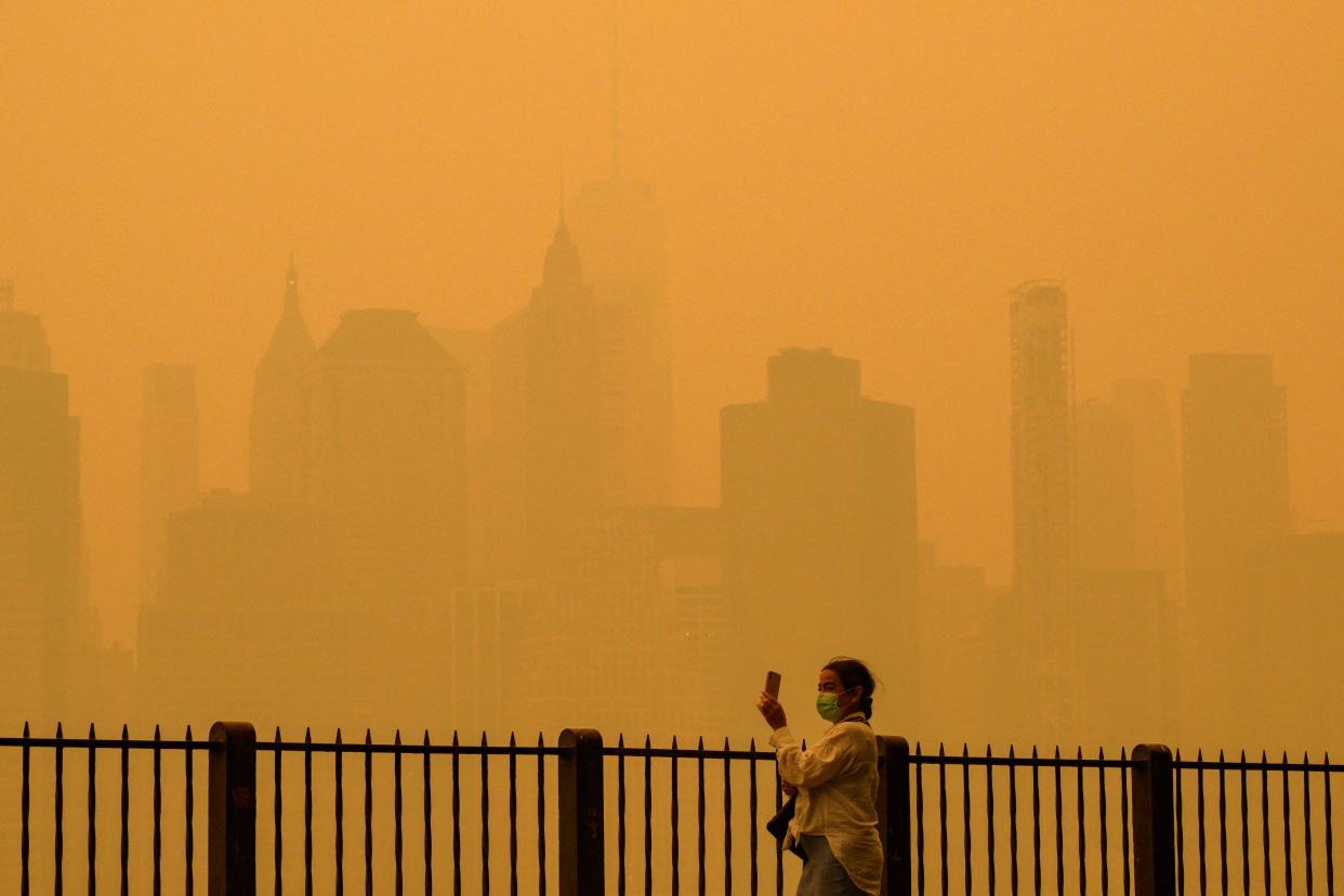 A person wearing a face mask takes photos of the skyline as smoke from wildfires in Canada cause hazy conditions in New York City on June 7, 2023. An orange-tinged smog obscured its famous skyscrapers, causing residents to wear face masks, as cities along the US East Coast issued air quality alerts.