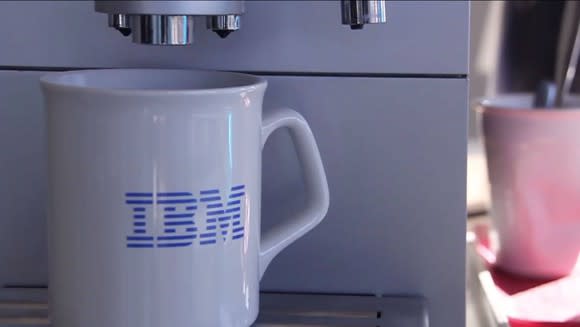 White coffee mug with blue IBM logo on it under an espresso machine.