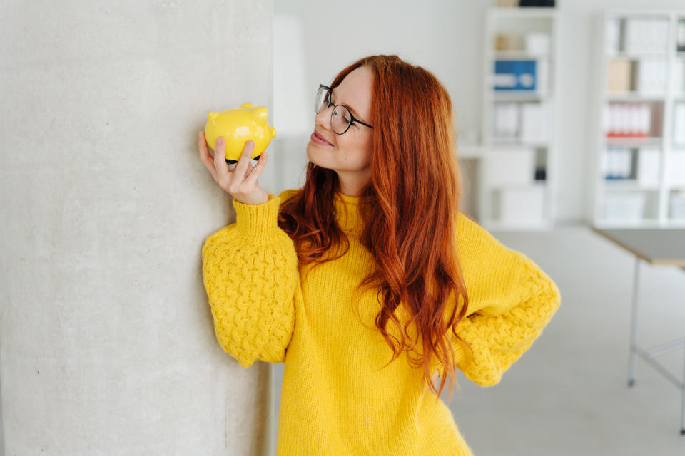 Smiling young businesswoman contemplating a piggy bank