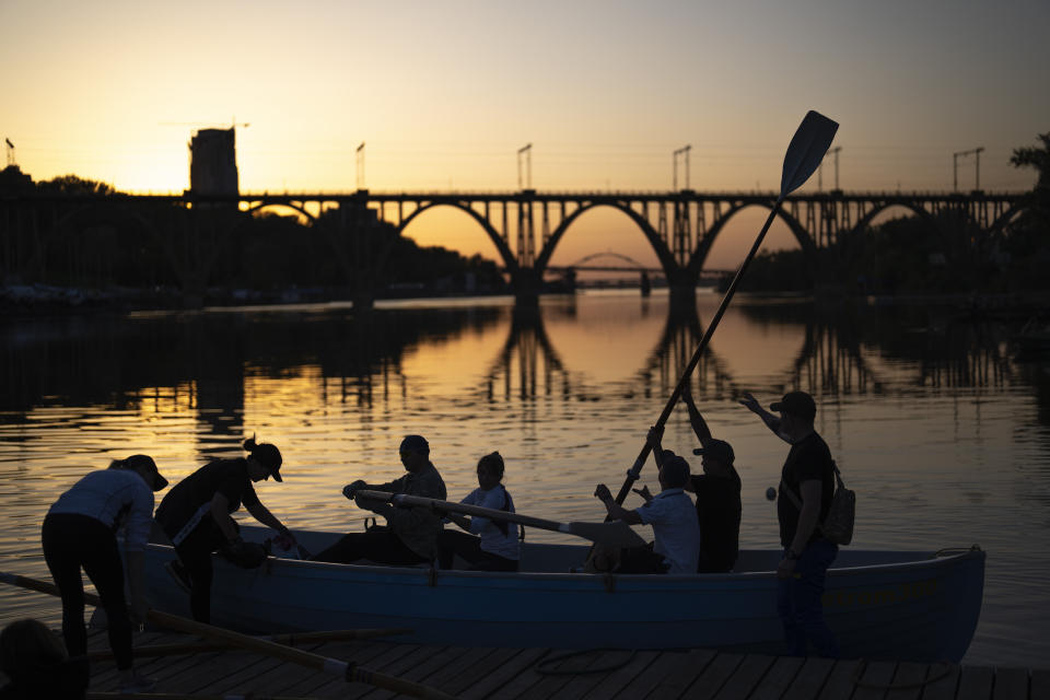 FILE - Ukrainians, a few of them displaced from Mariupol during the war, practice rowing on the Dnipro River as the sun sets, in Dnipro, Ukraine, Thursday, May 2, 2024. The southern city of Kherson section of the Dnipro is now the only natural barrier between Ukrainian and Russian troops in the region, with drones, artillery and missiles are flying overhead daily and mines in the water. (AP Photo/Francisco Seco, File)