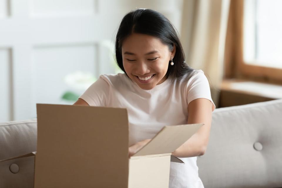 A person smiles while sitting on a couch and opening a package. 