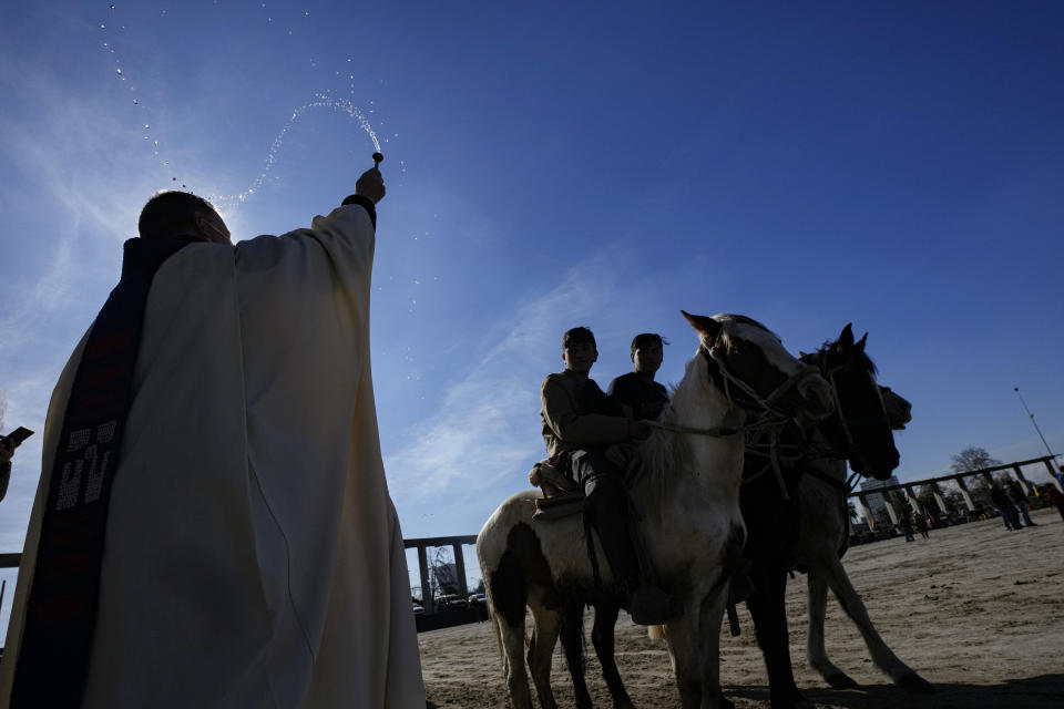 Un sacerdote bendice con agua bendita" a jinetes durante la celebración en honor de la Virgen del Carmen, patrona de Chile, frente al Santuario Nacional de Maipú, en Santiago, el sábado 16 de julio de 2022. (AP Foto/Esteban Felix)