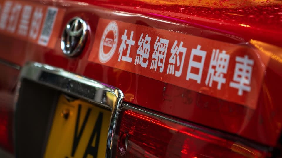 A sticker reading "Eliminate online booking of white-plate vehicles" is seen on the back of a taxi in Hong Kong, China, on May 24, 2024. - Noemi Cassanelli/CNN