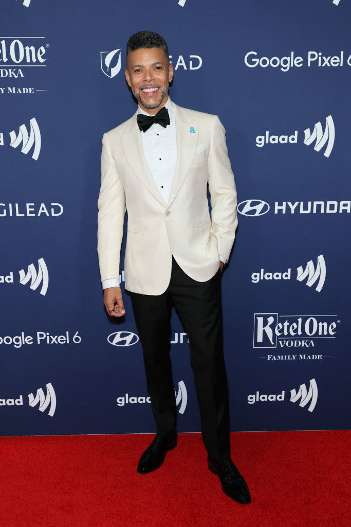 Wilson Cruz standing and smiling at a step-and-repeat