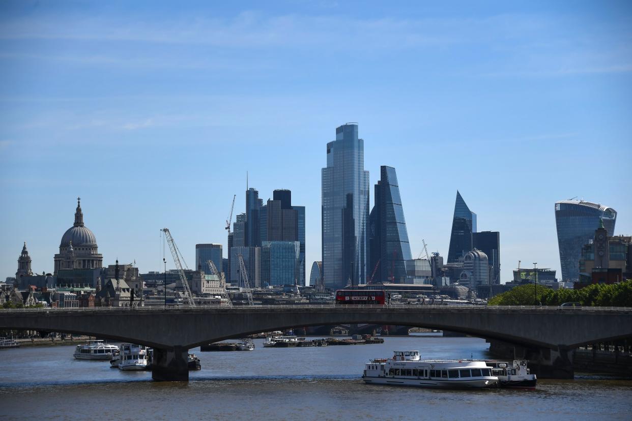 Buses drive across Waterloo Bridge, against the backdrop of the City of London' skyline in London, on Monday, May 18, 2020. Britain's Prime Minister Boris Johnson announced last Sunday that people could return to work if they could not work from home.