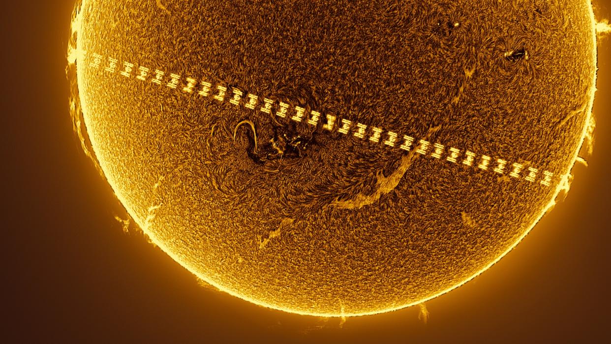  A t-shaped space station passes in front of a fiery sun. 