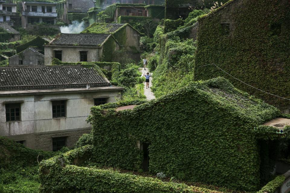 Tourists walk between buildings covered with vines in the abandoned fishing village of Houtouwan on the island of Shengshan July 26, 2015. (REUTERS/Damir Sagolj)