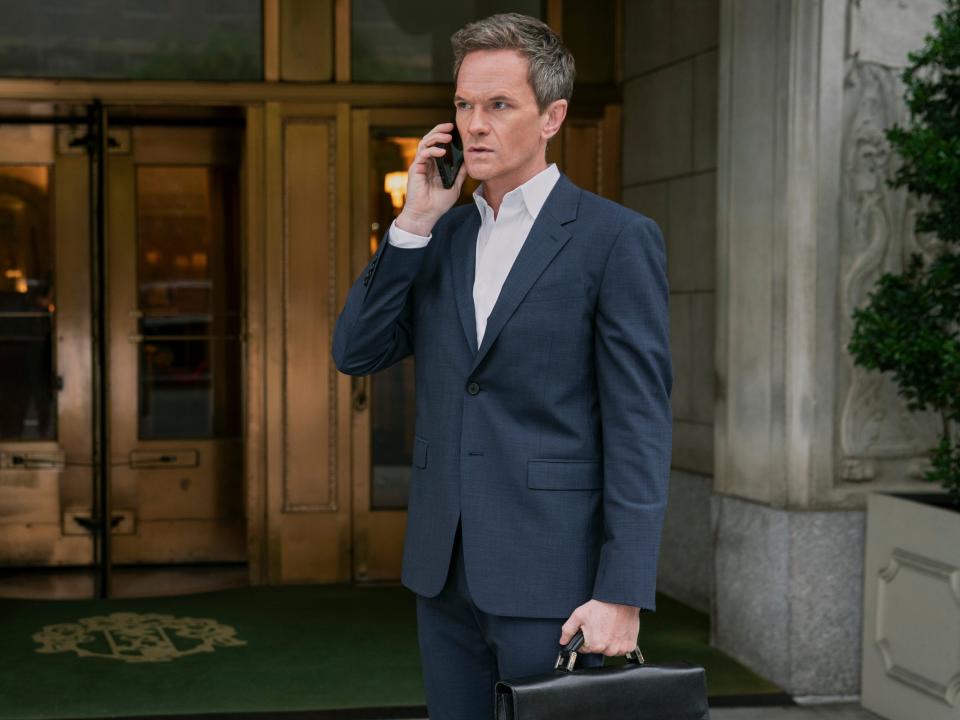 Neil Patrick Harris standing on the phone with a blue suit and briefcase