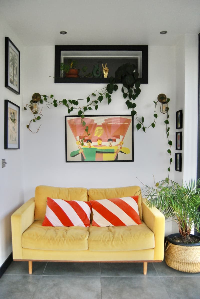 Yellow couch below-framed artwork and plants.